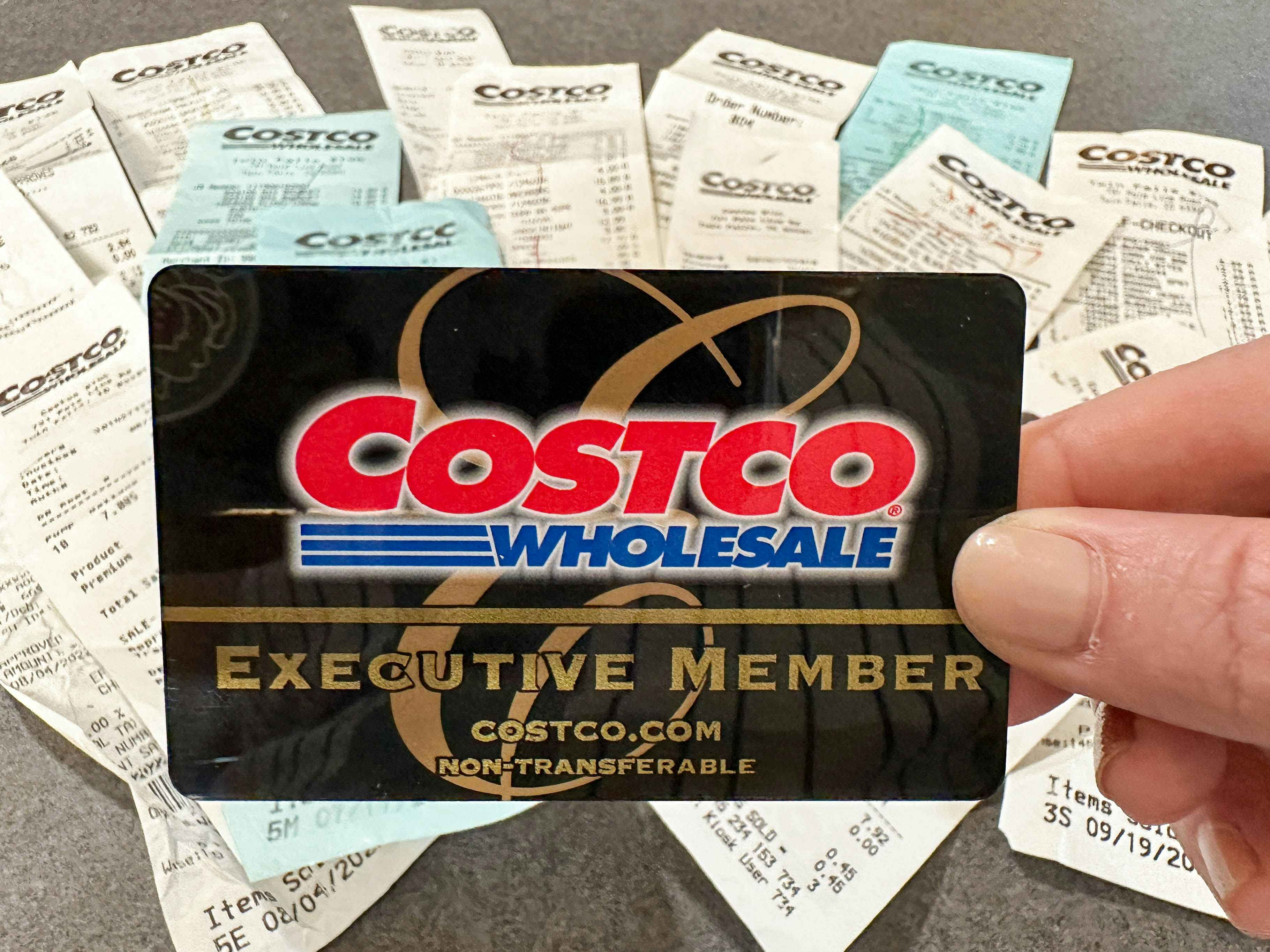 a person holding up a costco card in front of a bunch of receipts