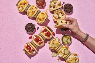 four ihop breakfast tacos set against a pink background with a hand grabbing one of the tacos