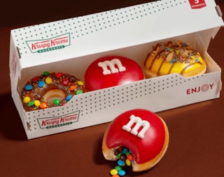 a three pack of krispy kreme m&m doughnuts against a brown background