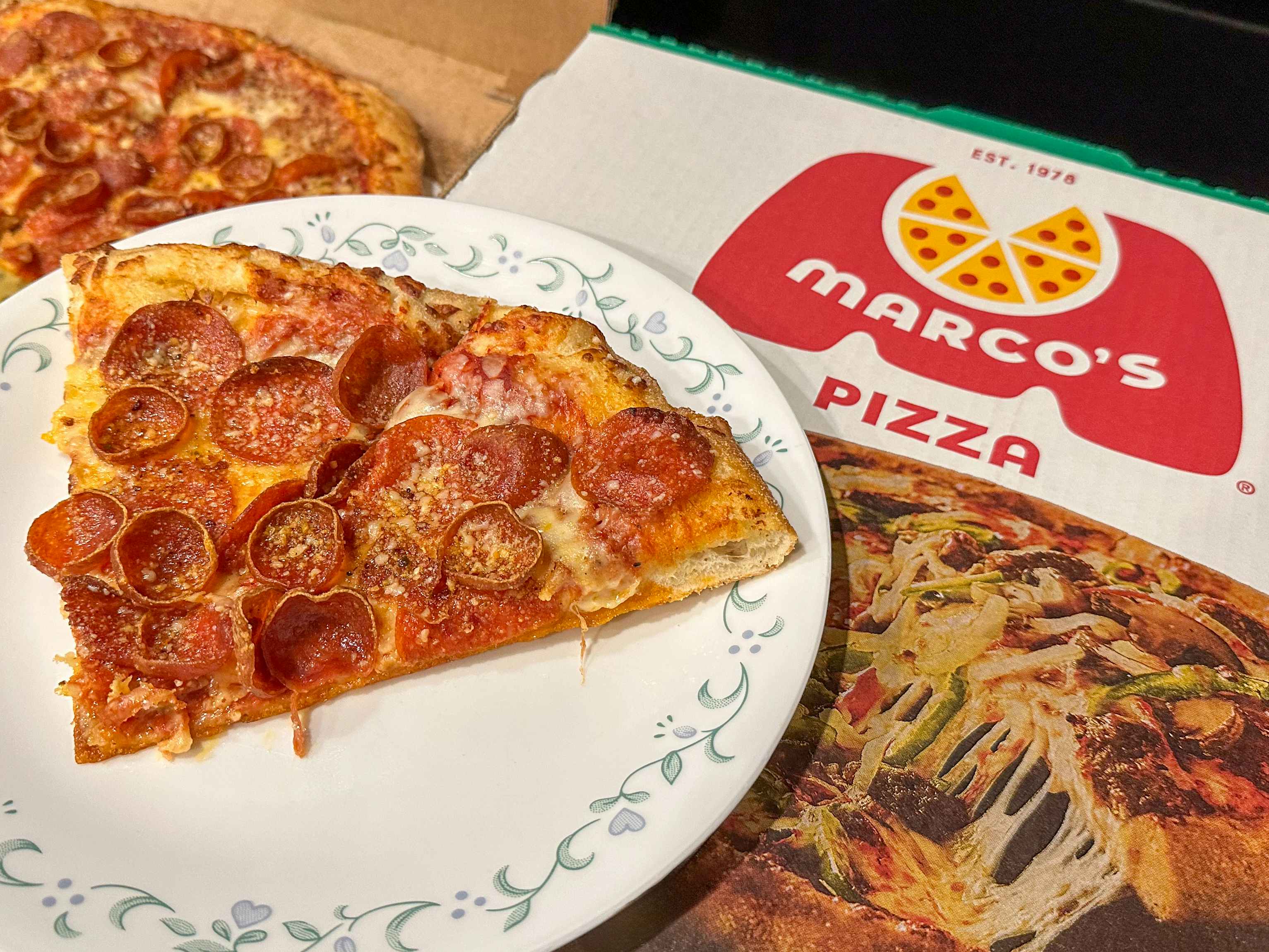 pieces of pizza on a plate on top of a Marco's Pizza box