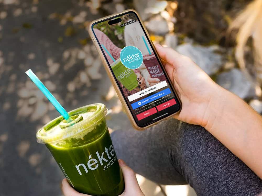 Someone looking at the Nekter app while holding a smoothie from the Nekter Juice Bar