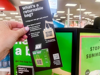 Someone holding up a returnable bag brochure next to a sign in Target