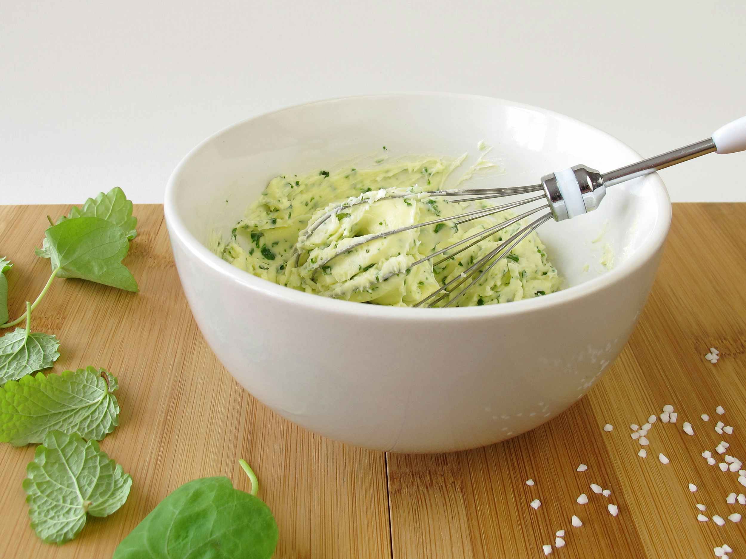 bowl of compound butter with whisk, herbs, and salt