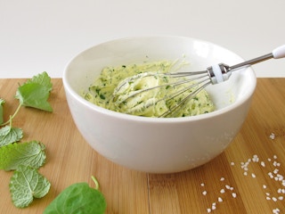 bowl of compound butter with whisk, herbs, and salt