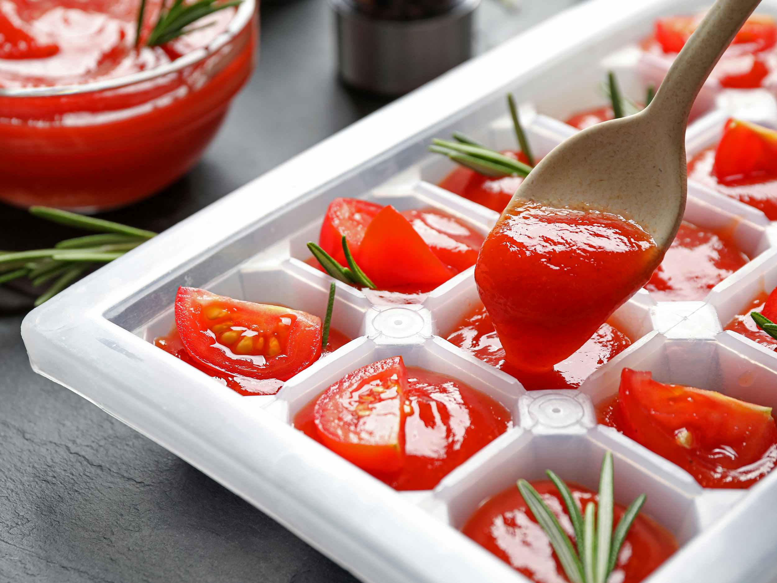 spoon adding tomato sauce to ice cube tray for freezing