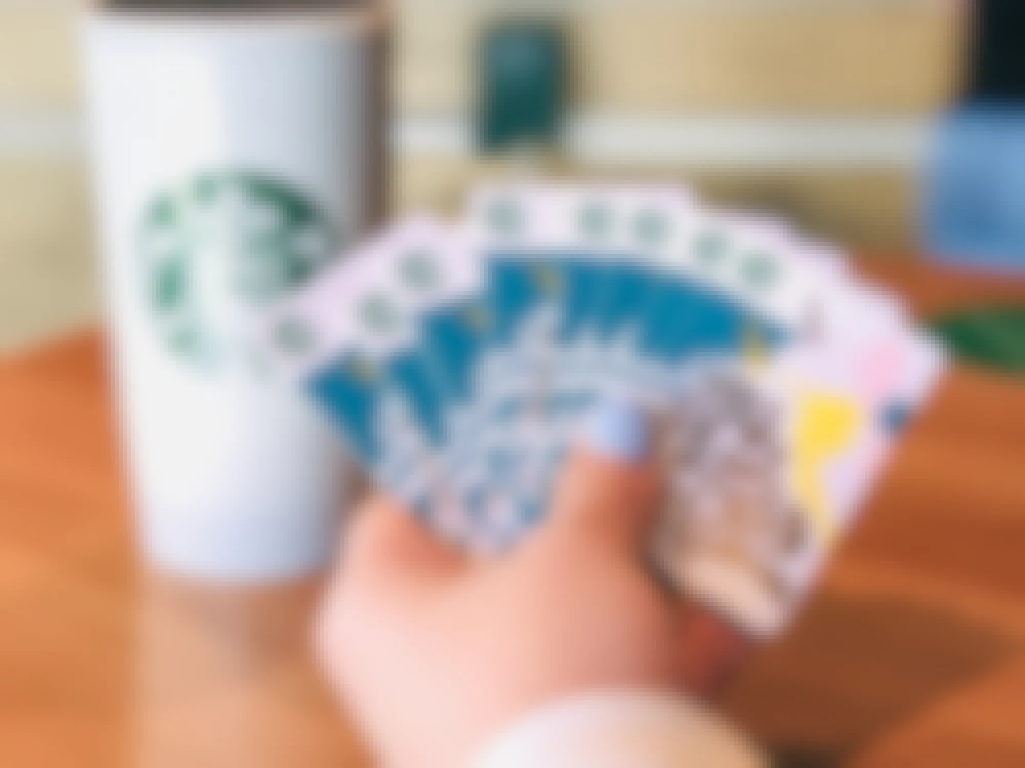 Someone holding a fan of gift cards in front of a starbucks cup