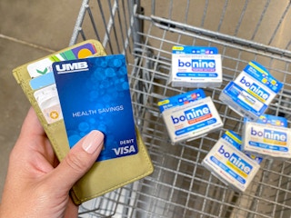 person holding wallet and hsa debit card with bonine meclizine products in walmart shopping cart