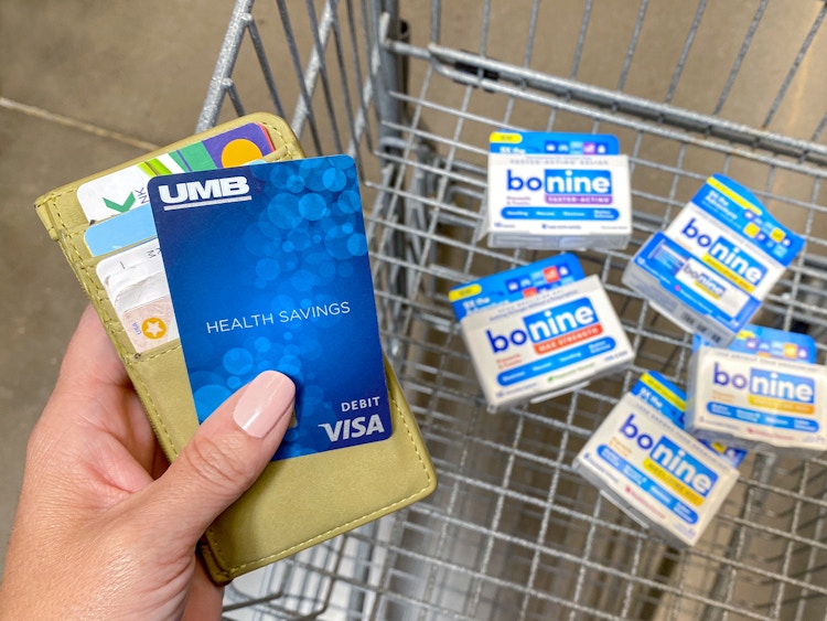 person holding wallet and hsa debit card with bonine meclizine products in walmart shopping cart