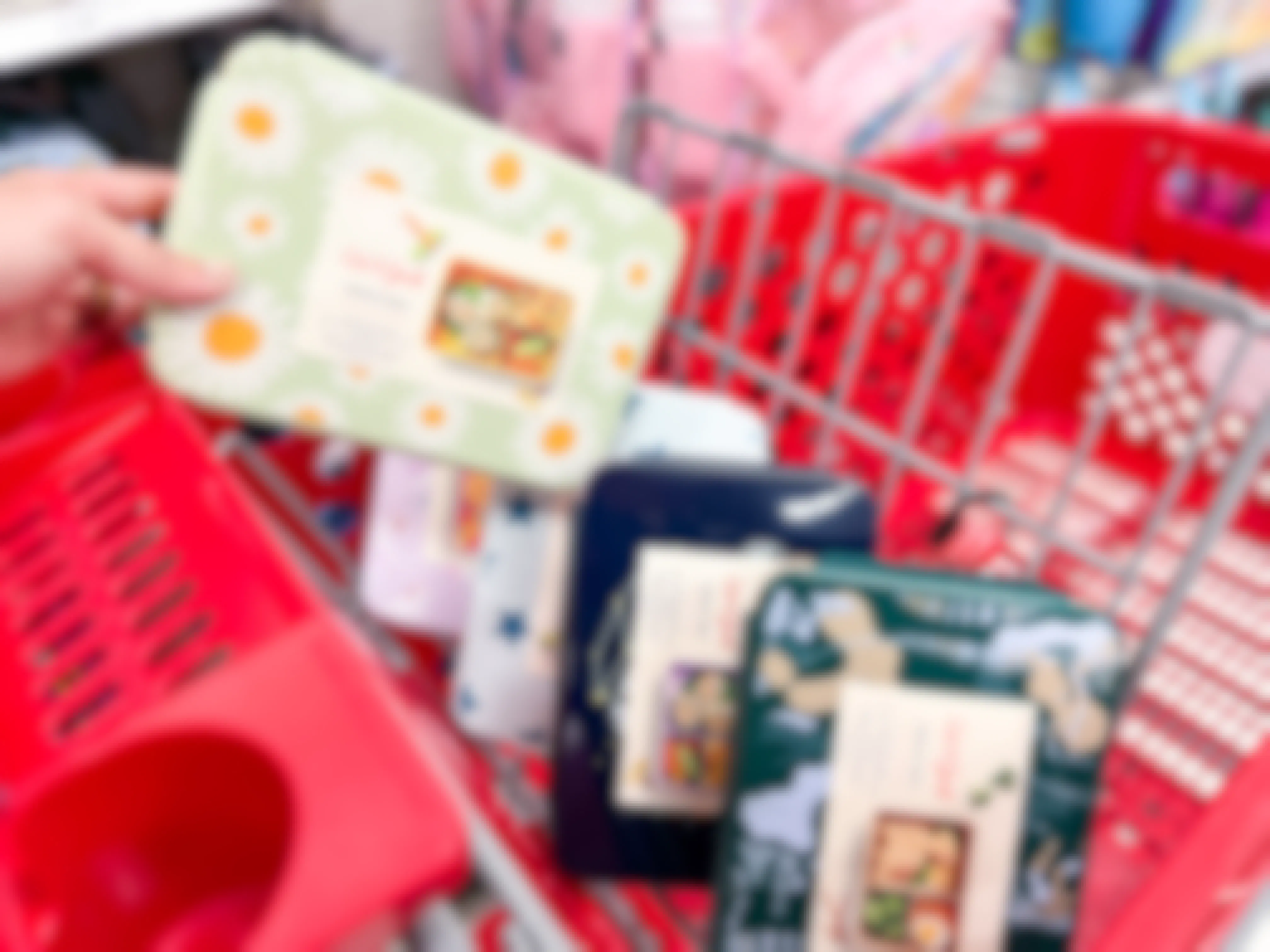 a woman's hand putting a target cat and jack bento box with daisies on it into her shopping cart with three other bento boxes in the cart already