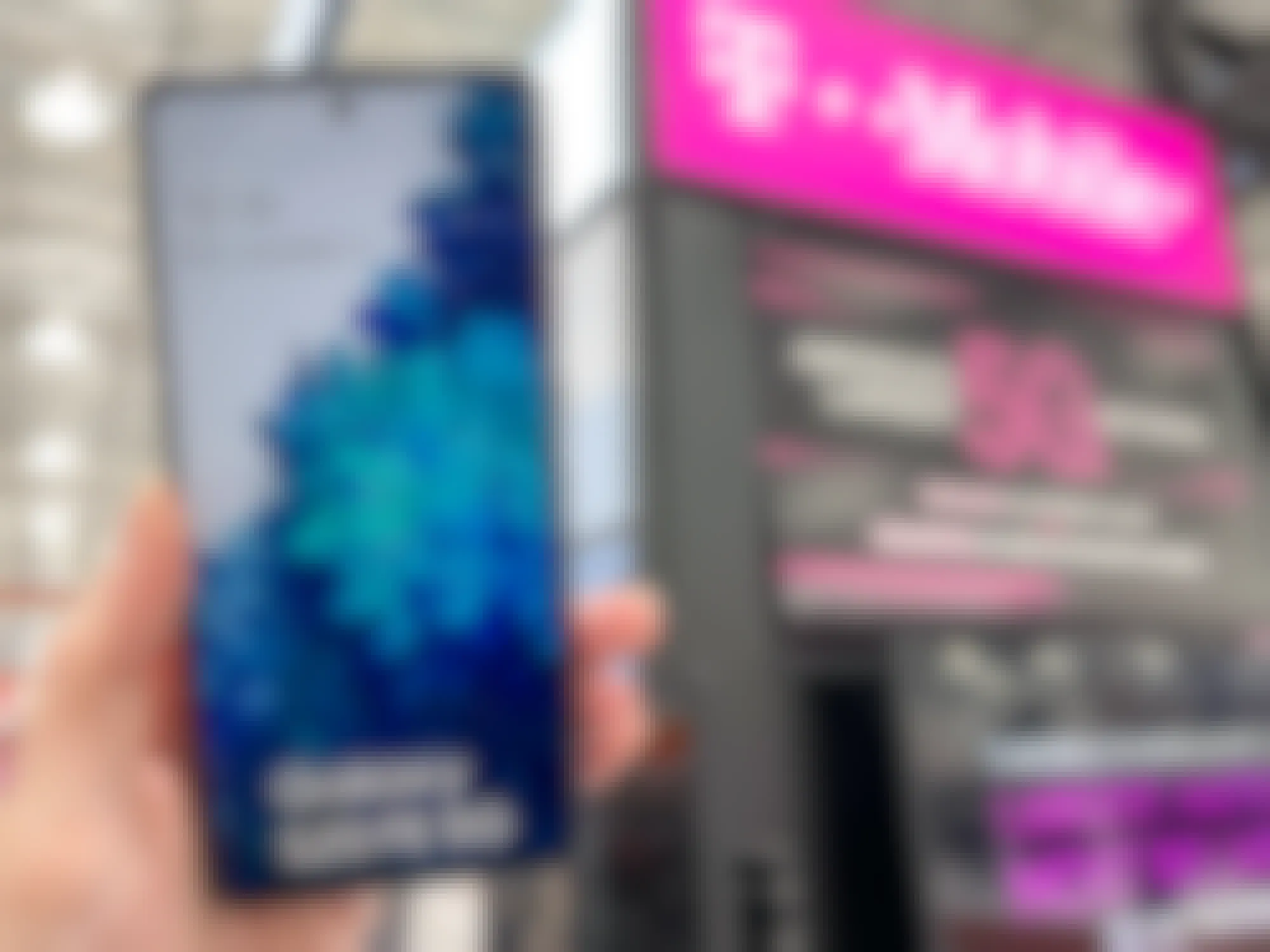 Someone holding up an android phone in front of a T-Mobile sign