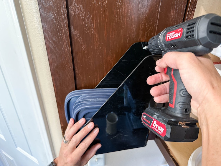 a person screwing a plastic magazine holder to a cupboard door