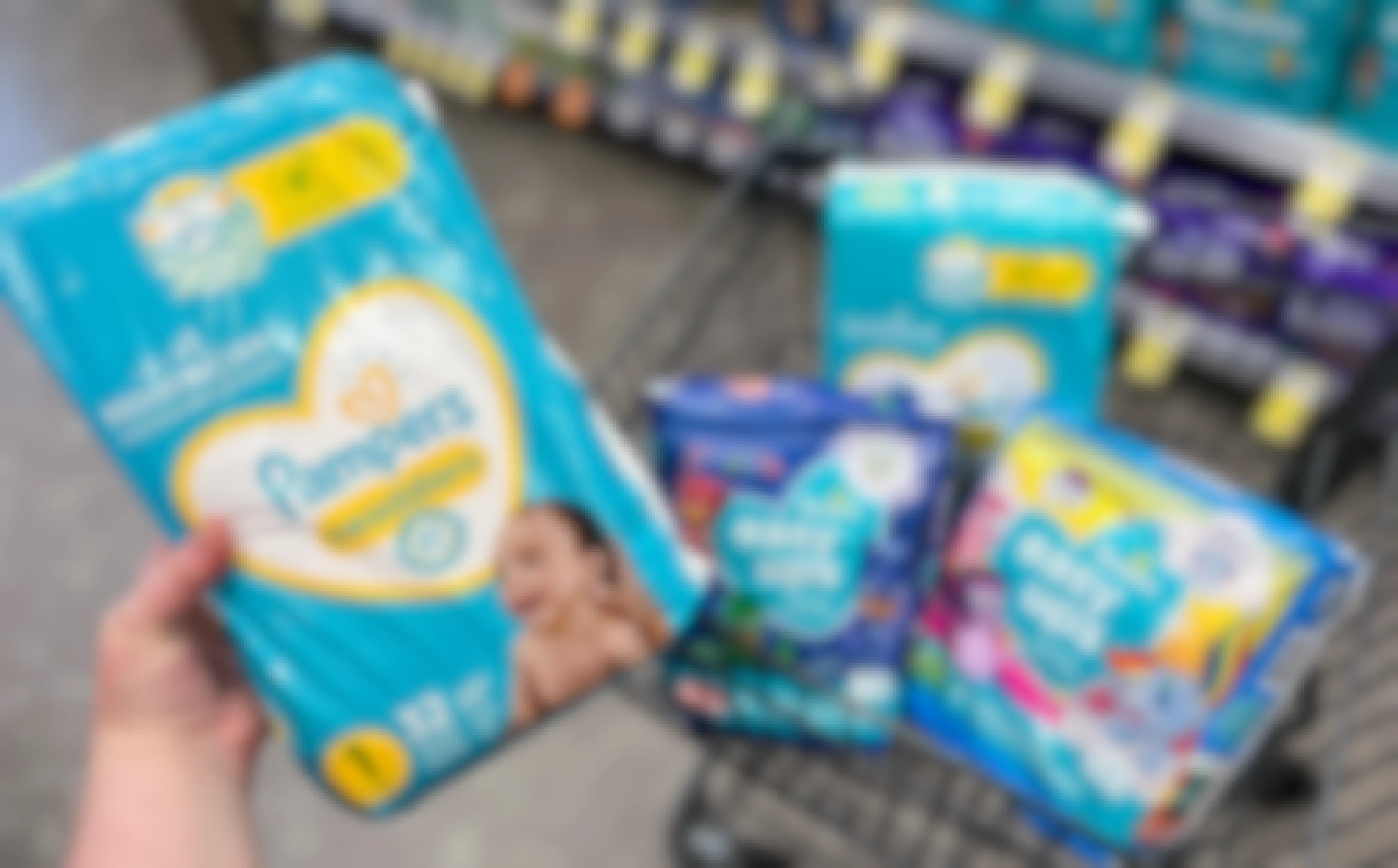 hand holding pampers diapers with a walgreens cart filled with more packs of pampers diapers and easy ups