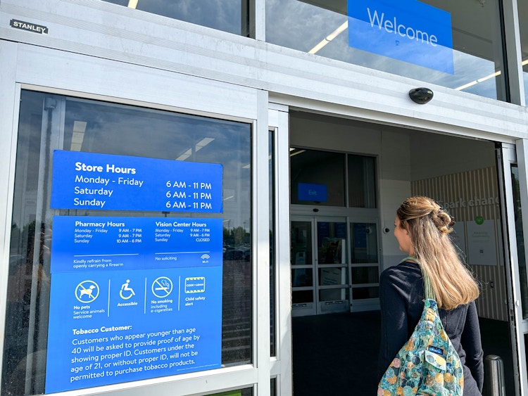 a person walking into a walmart store with the hours on the door 