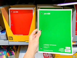 person holding green pen+gear college-ruled spiral notebook near walmart shelf