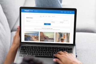 a woman lying on the couch with her laptop looking at the Walmart Plus Travel page online