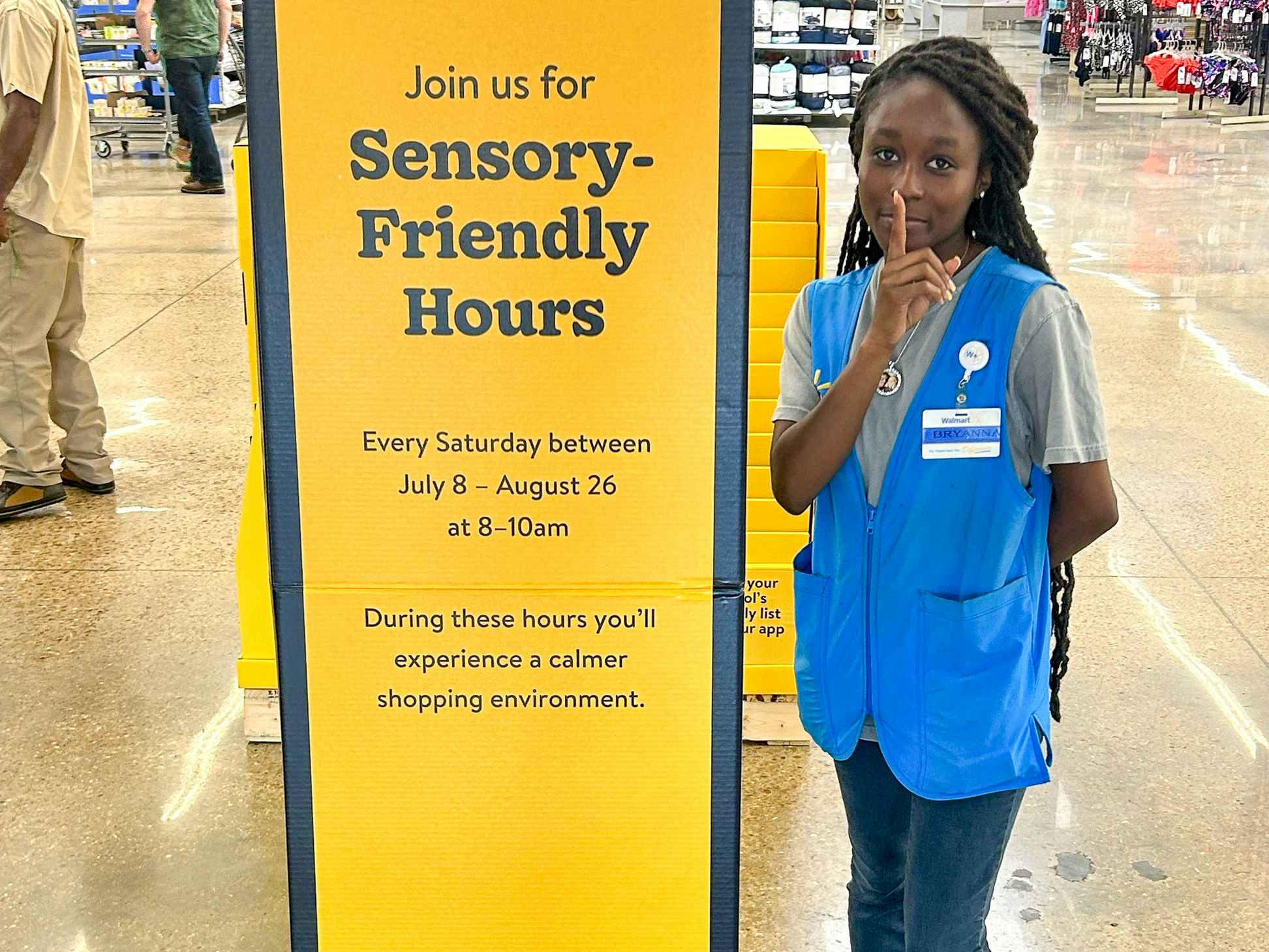 A Walmart employee standing next to a sign inside Walmart advertising their Sensory-Friendly store hours