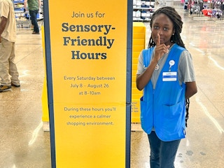 A Walmart employee standing next to a sign inside Walmart advertising their Sensory-Friendly store hours