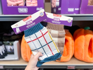 a person holding up two aldi pet sweaters