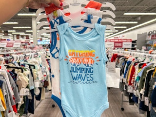 a person holding up baby bodysuits in a burlington store