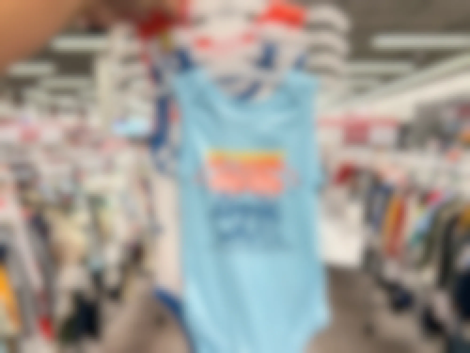 a person holding up baby bodysuits in a burlington store
