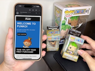 someone holding up a phone displaying a coupon for the Funko website next to some Funko POP Vinyls