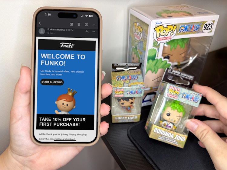 someone holding up a phone displaying a coupon for the Funko website next to some Funko POP Vinyls