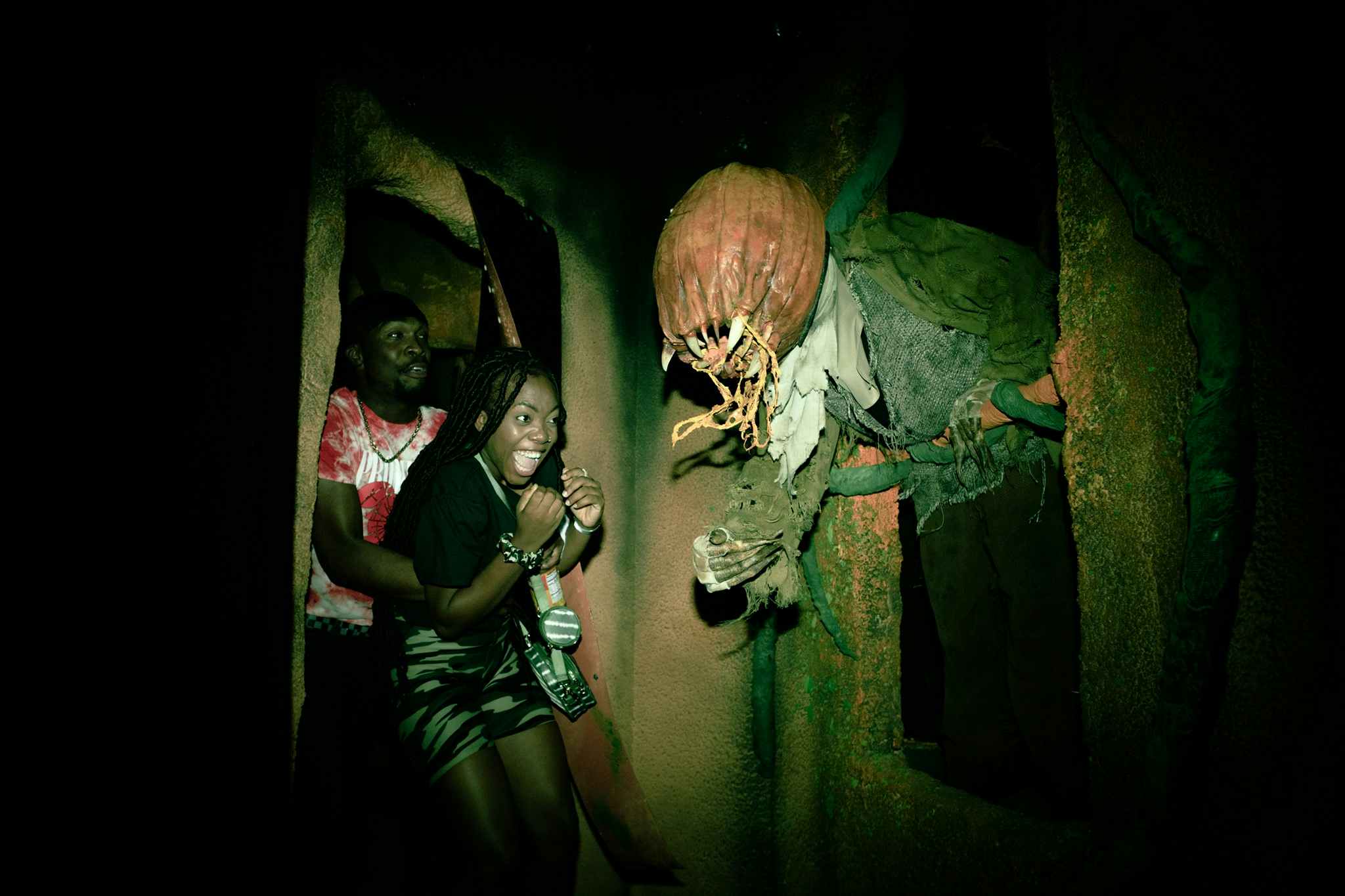 A couple walking through a haunted house getting scared by a figure with a pumpik head and sharp teeth