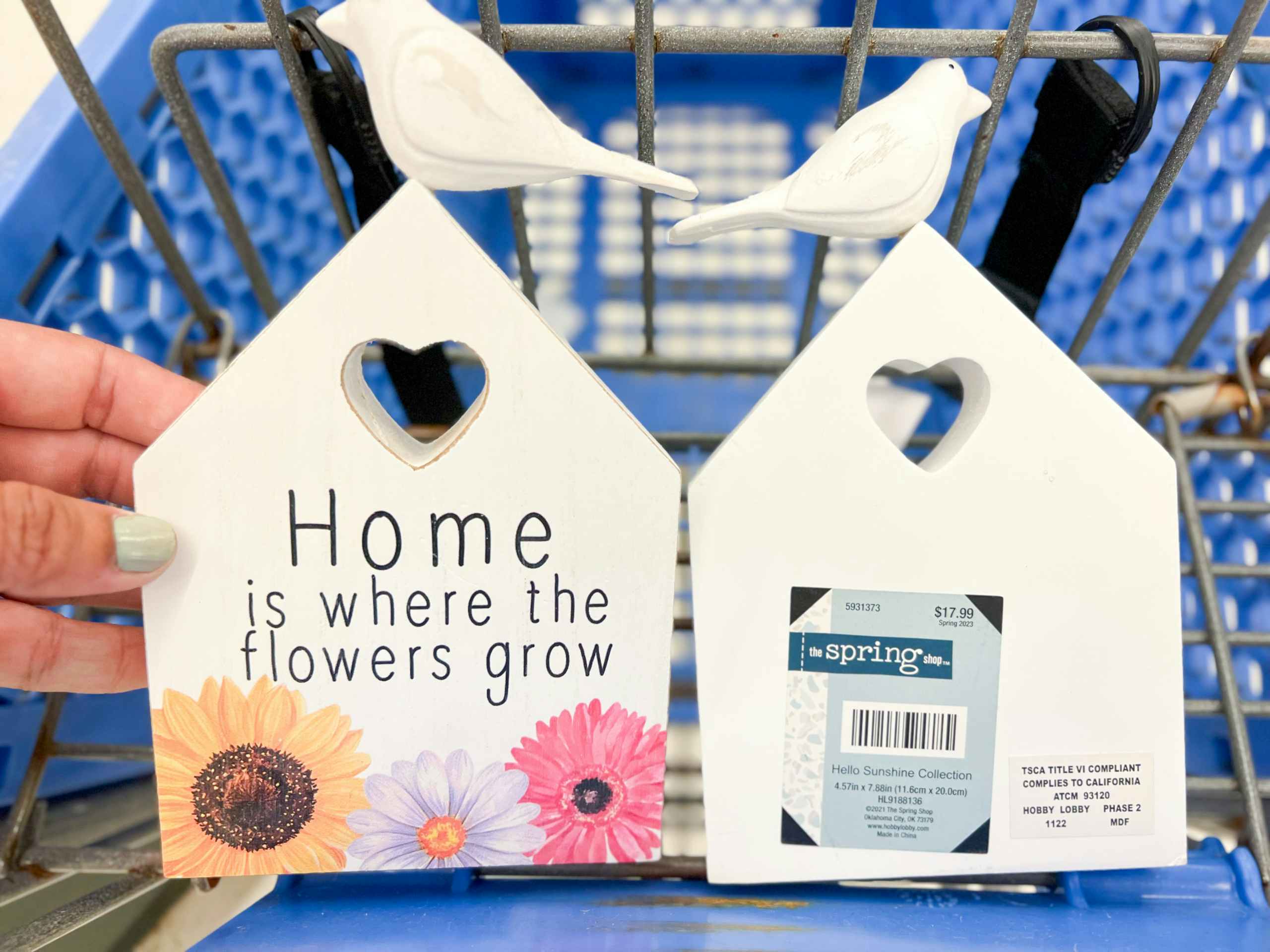 white wooden table decor in the shape of a house with "Home is where the flowers grow" on it sitting in a hobby lobby cart