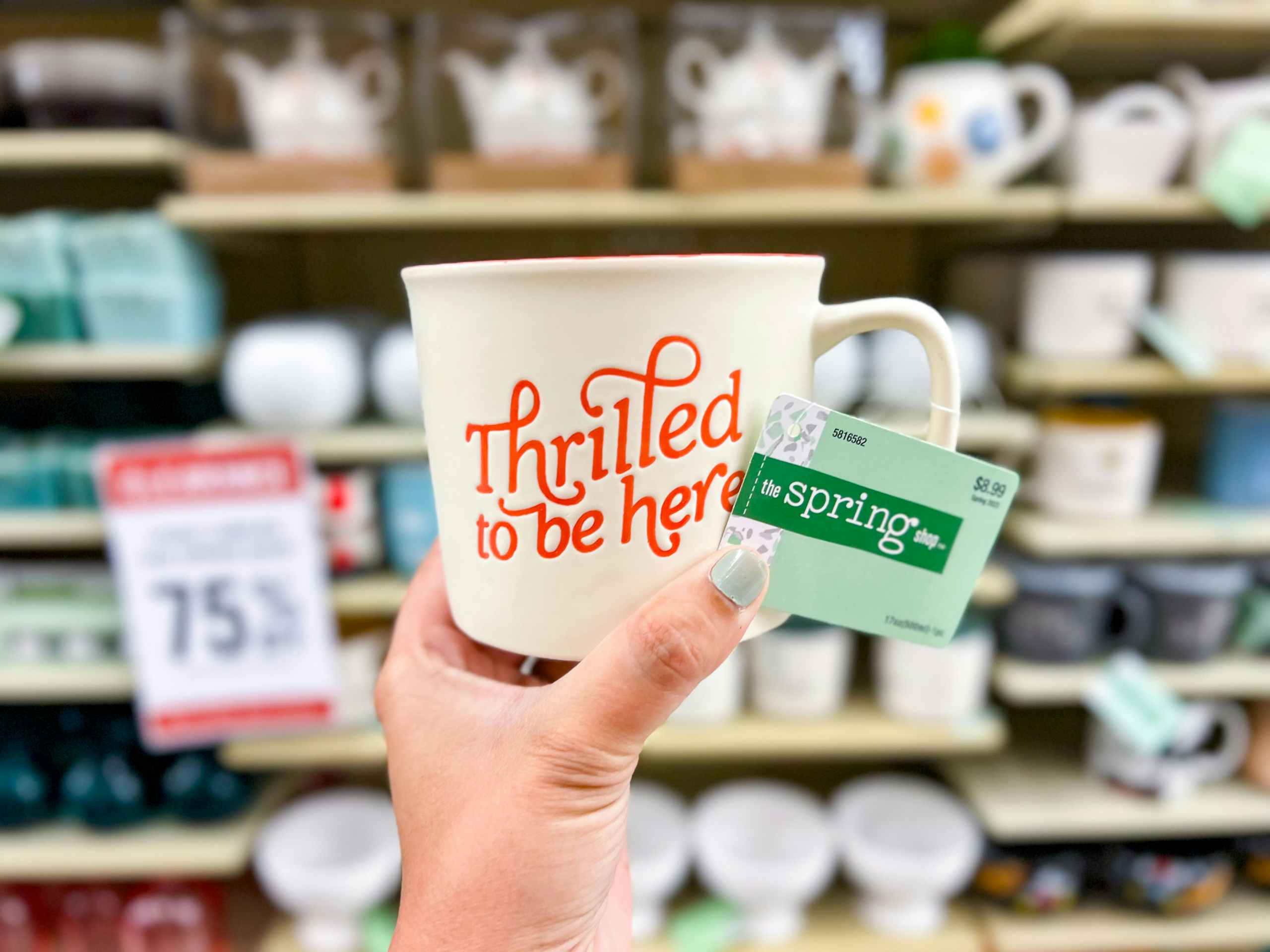 hand holding up a cream mug that says "thrilled to be here" in red cursive writing