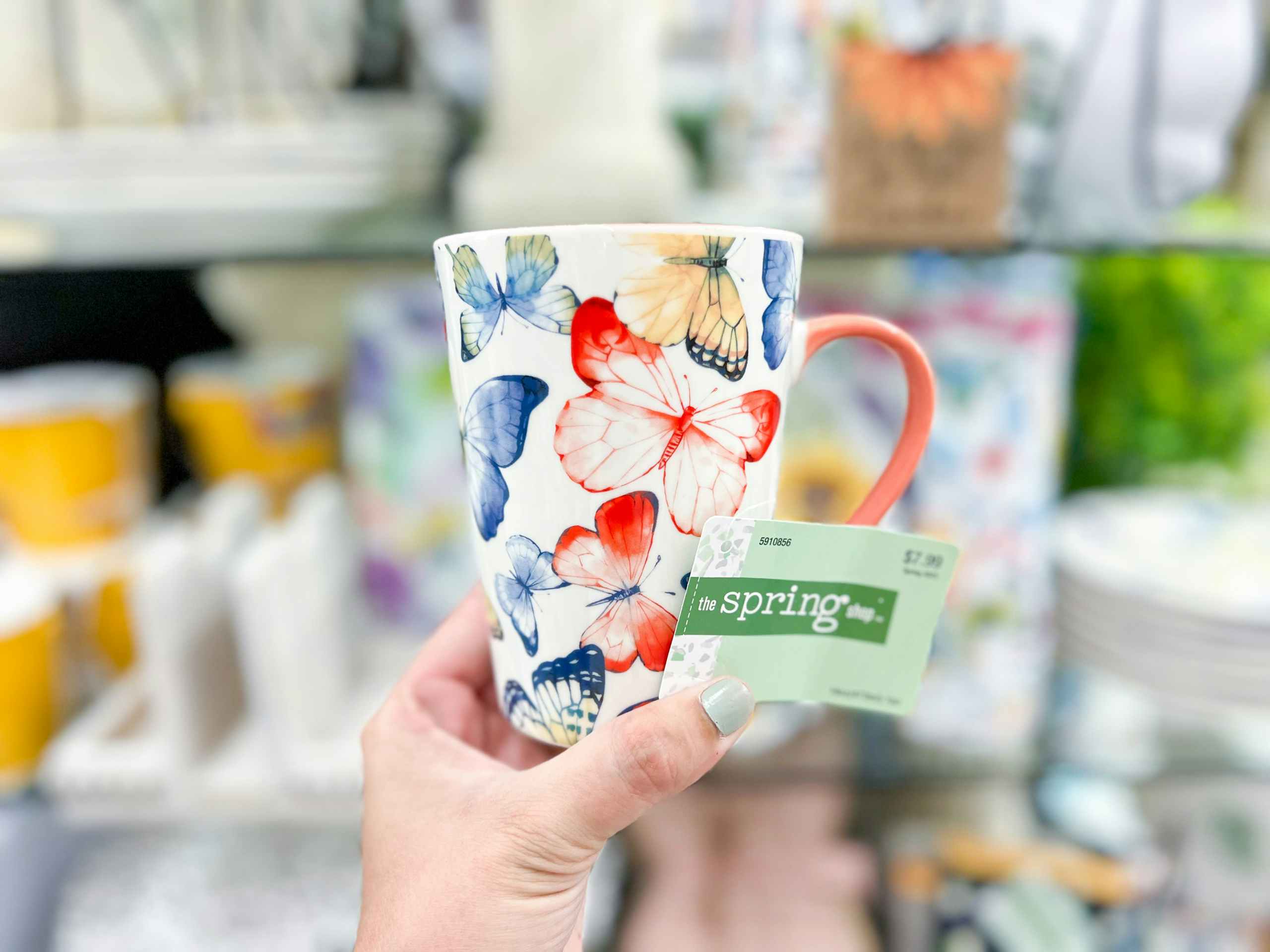 hand holding up a white mug with butterflies in multiple colors