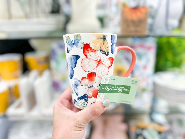 hand holding up a white mug with butterflies in multiple colors