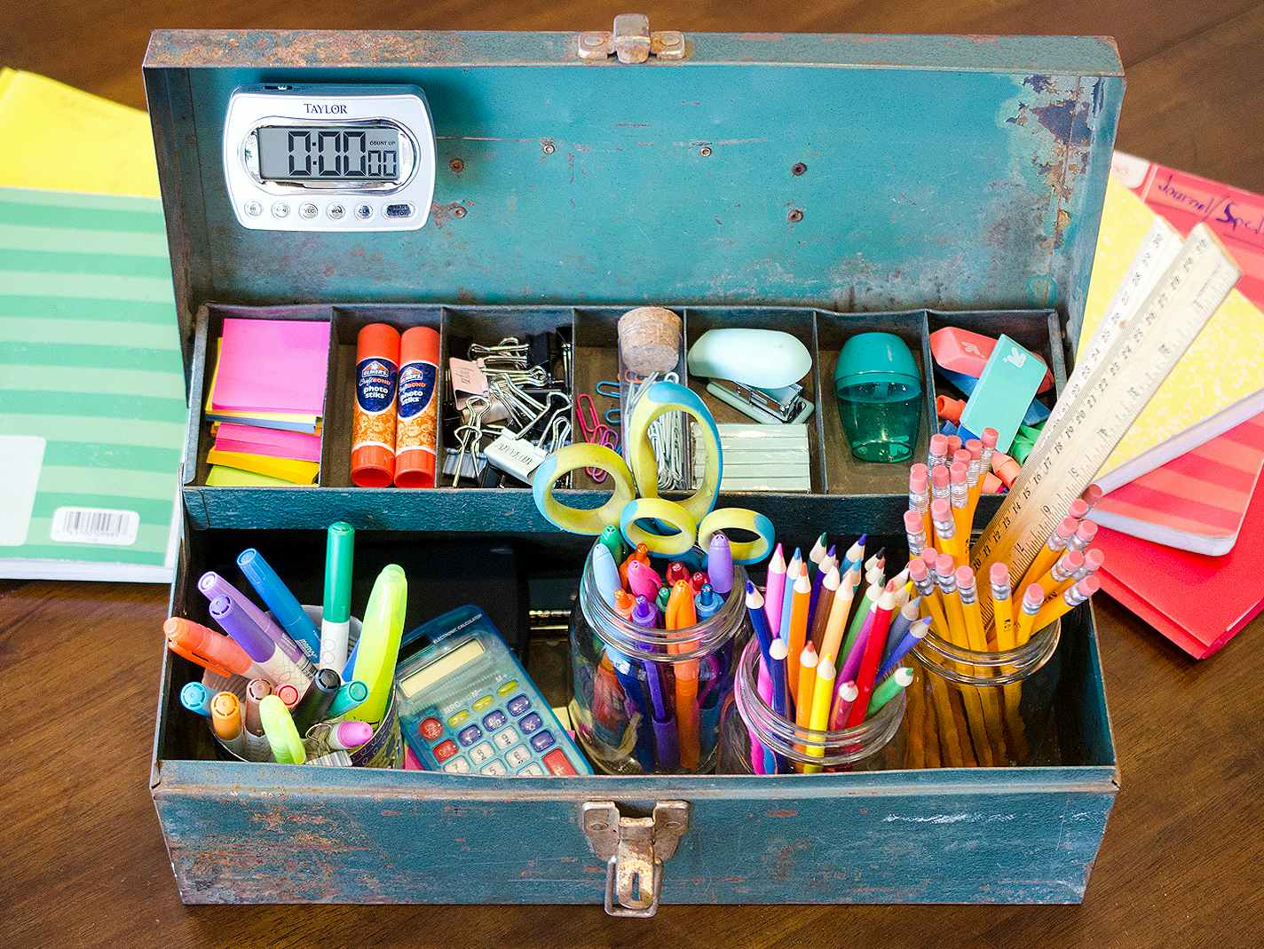 A toolbox full of school supplies sitting on a table in front of some notebooks.