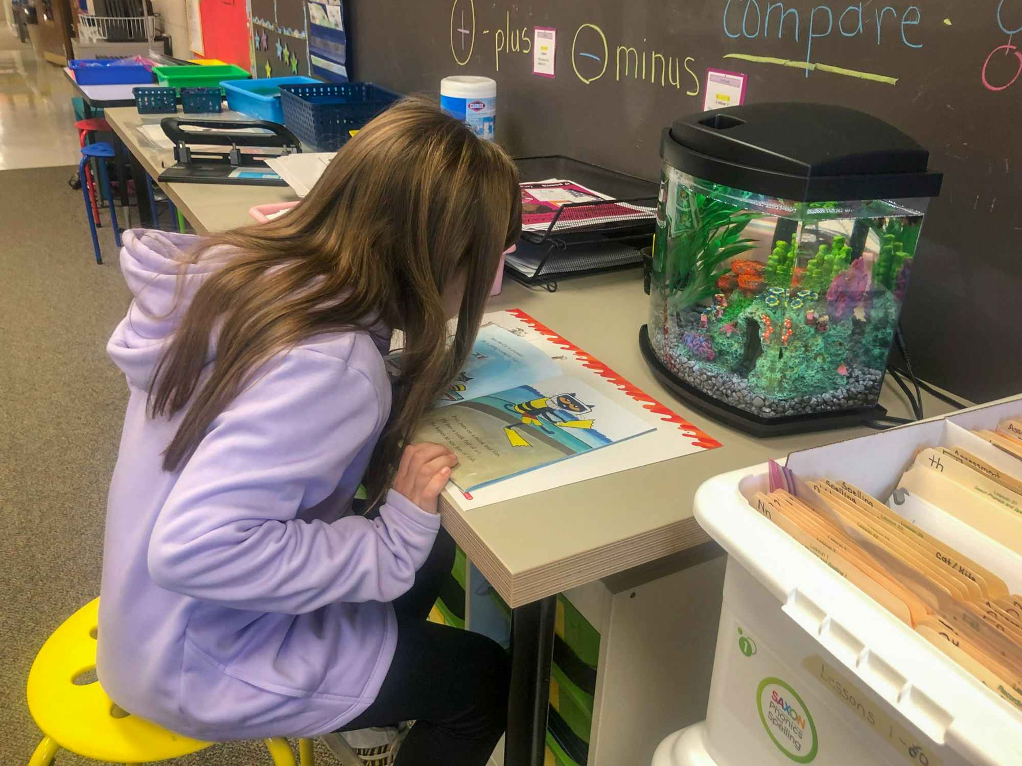 a student reading a book next to a fish tank in a classroom
