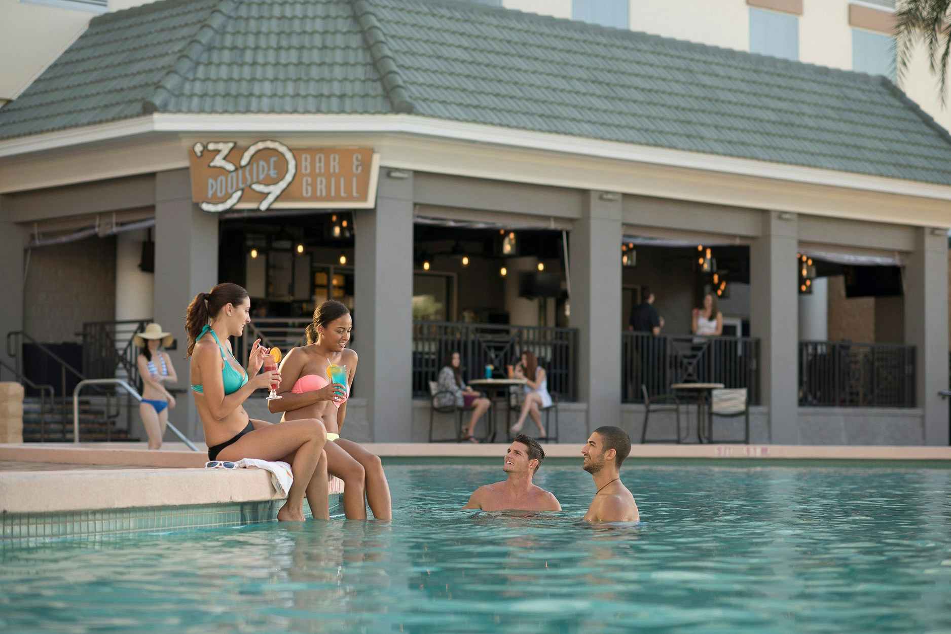 A group of friends hanging out in a pool next to a hotel restaurant