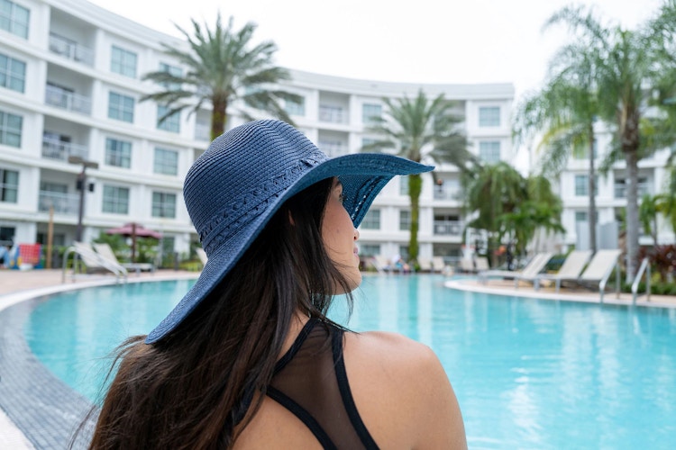 A woman sitting poolside with a sunhat