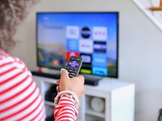 in striped shirt holding Roku remote near tv