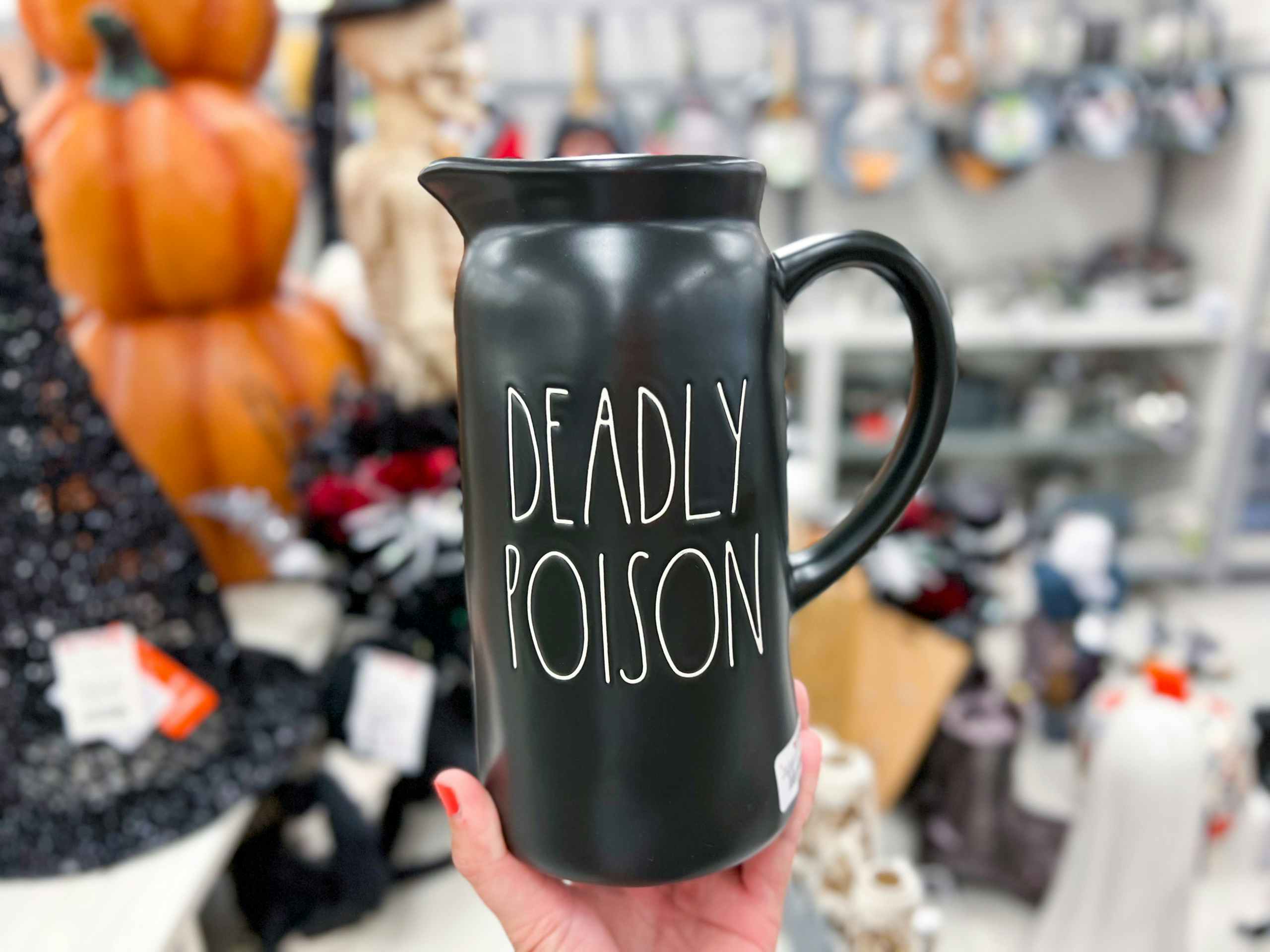 hand holding up a black rae dunn pitcher that says "deadly poison