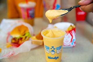 Scoop of Pumpkin Spice Fall Flavored frosty in the foreground with a chicken sandwich and drink in the background