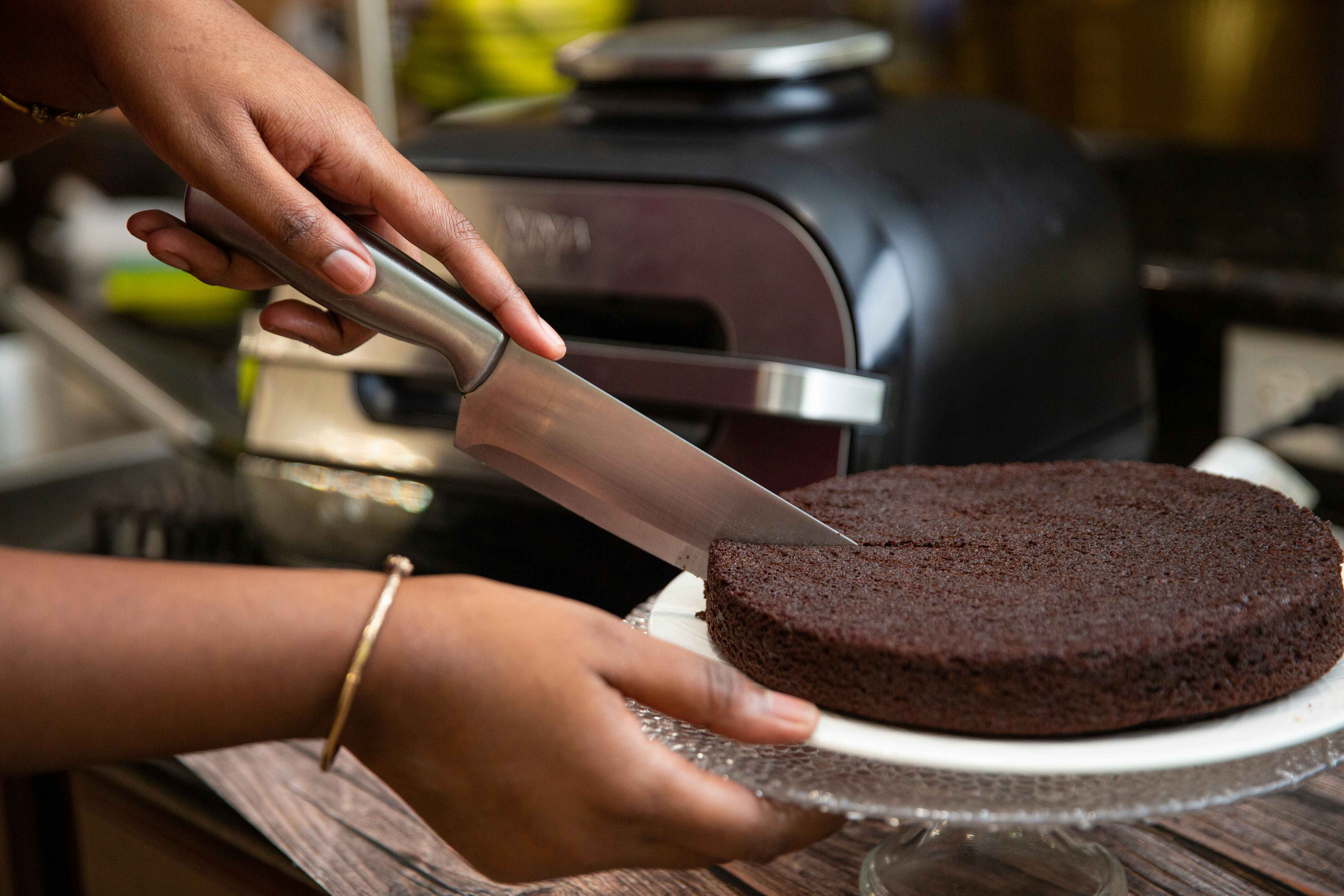 Hand cutting a chocolate cake in front of a silver and black air fryer