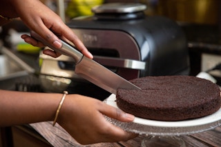Hand cutting a chocolate cake in front of a silver and black air fryer