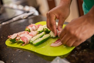 Hand wrapping a jalepeno stuff with mozzarella cheese with bacon on a green cutting board