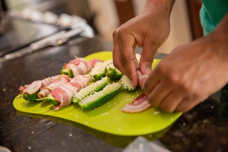 Hand wrapping a jalepeno stuff with mozzarella cheese with bacon on a green cutting board