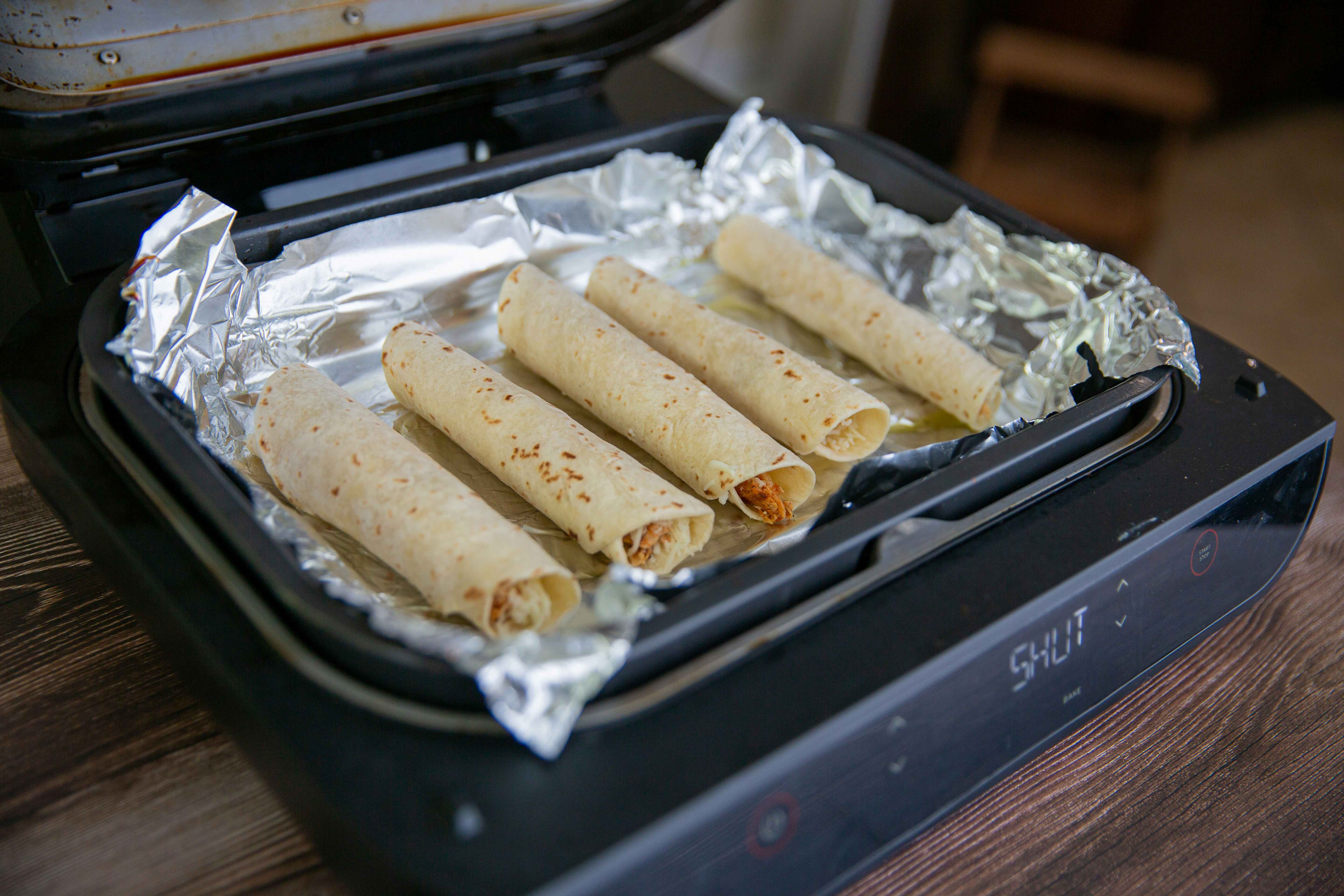 row of taquitos placed inside an aluminum lined airfryer