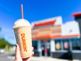 Person holding a drink in front of Dunkin Donut