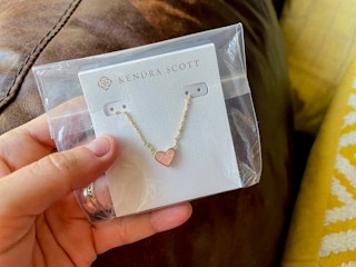 a person holding a kendra scott necklace