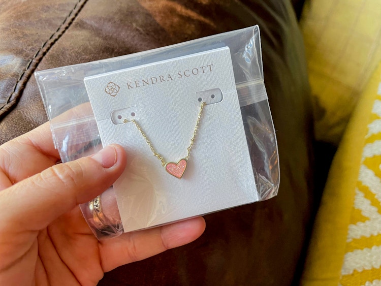 a person holding a kendra scott necklace