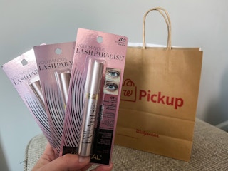 hand holding three loreal lash paradise mascaras in front of online pickup shopping bag