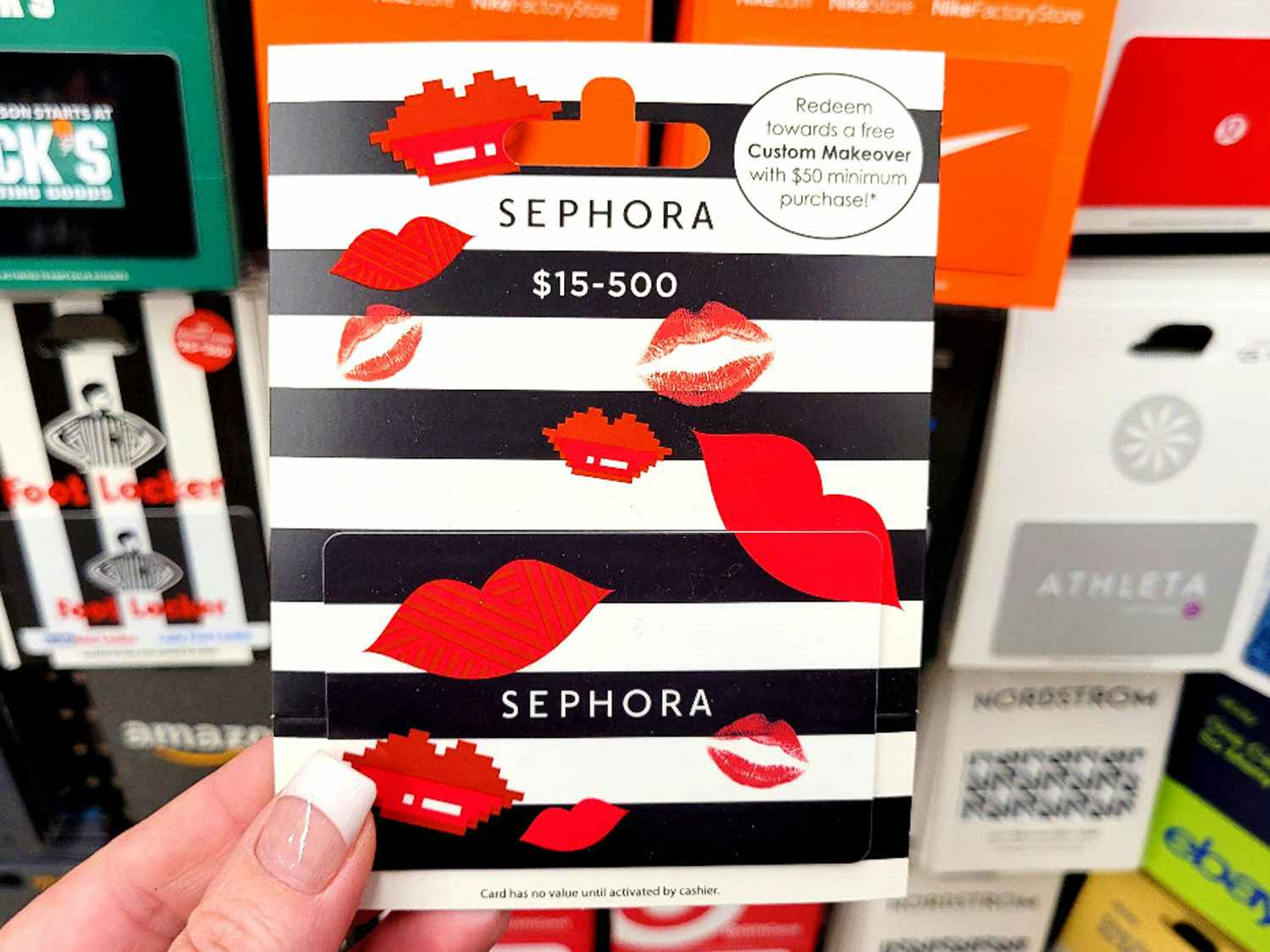 A person's hand holding a Sephora gift card in front of a display of gift cards 