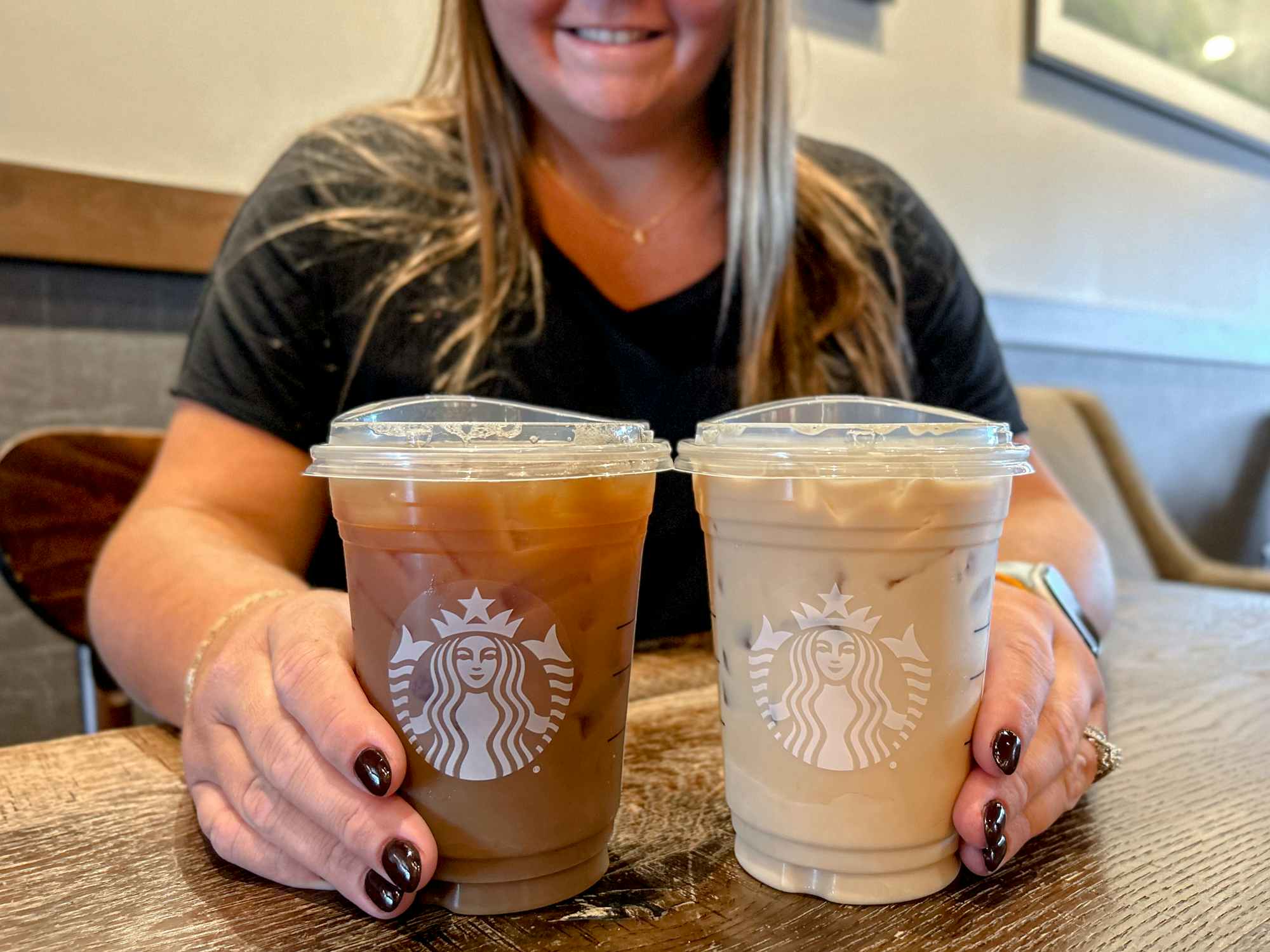 a person smiling while holding two iced coffee drinks at starbucks