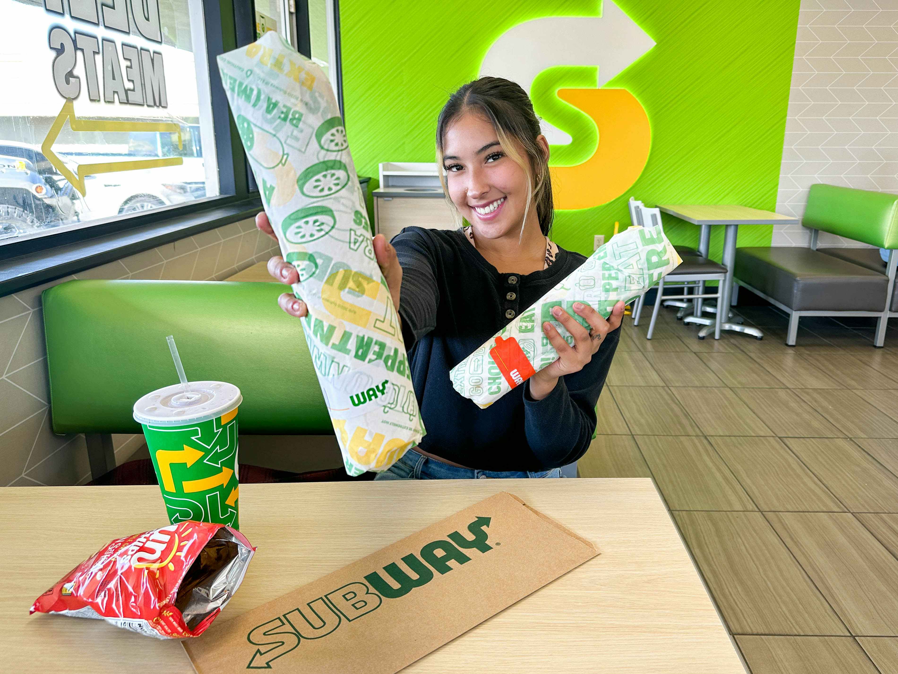 a woman holding out subway sandwiches